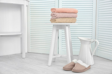 Beautiful composition with clean towels, slippers and jug in light room