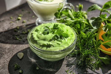 Delicious yogurt sauce in bowl with ingredients on table, closeup