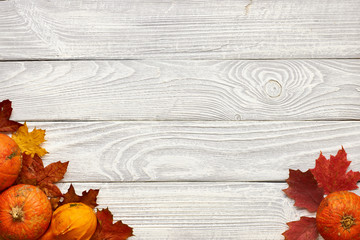 Autumn leaves and pumpkins over old wooden background