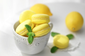 Cup with tasty lemon macarons on table, closeup
