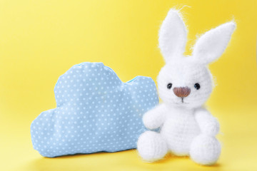 Cute handmade bunny toy with pillow in shape of cloud on color background, closeup