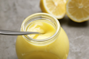 Glass jar with delicious lemon curd on gray table