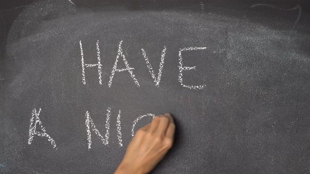 Woman's hand writing "HAVE A NICE DAY" with white chalk on blackboard