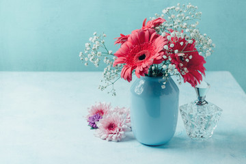 Flowers in vase with women perfume over blue background
