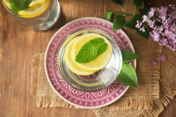 Glass with refreshing lemon water on beautiful plate