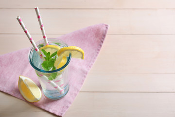 Refreshing lemon water in glass with straw on cute napkin