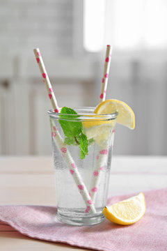 Refreshing lemon water in glass with straw on cute napkin