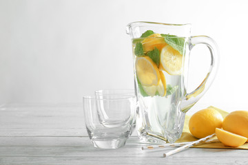 Jug and glasses with refreshing lemon water on wooden table