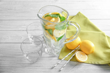 Jug and glasses with refreshing lemon water on wooden table