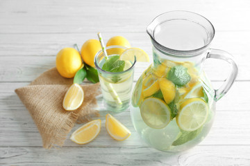Jug and glass with refreshing lemon water on wooden table