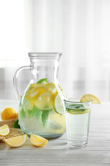 Jug and glass with refreshing lemon water on wooden table