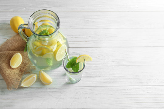 Jug and glass with refreshing lemon water on wooden table