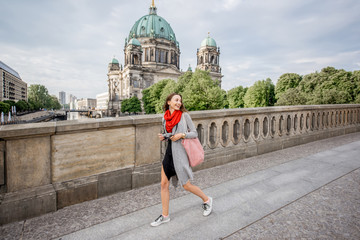 Young woman tourist with photo camera enjoying traveling in Berlin city walking on the old bridge near the famous cathedral - obrazy, fototapety, plakaty