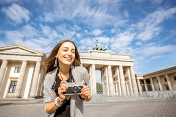 Portrait of a young smiling woman tourist standing with photo camera in front of the famous Brandenburg gates in Berlin