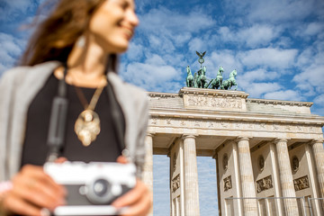Young woman tourist standing with photo camera in front of the famous Brandenburg gates in Berlin....