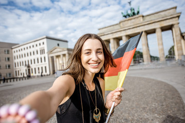 Young woman tourist making selfie photo with german flag standing in front of the famous Brandenburg gates in Berlin © rh2010