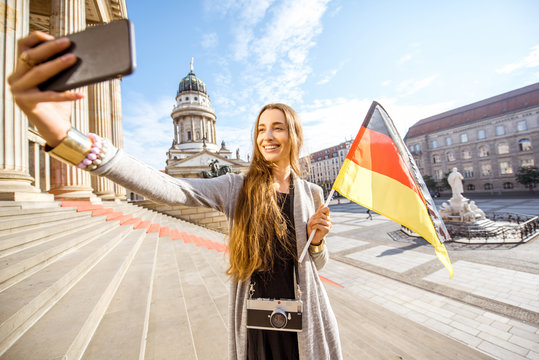 Young woman tourist making selfie photo standing with german flag on the stairs near the Concert house in Berlin