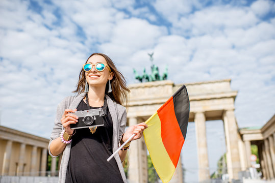 Portrait of a young smiling woman tourist standing with german flag in front of the famous Brandenburg gates in Berlin