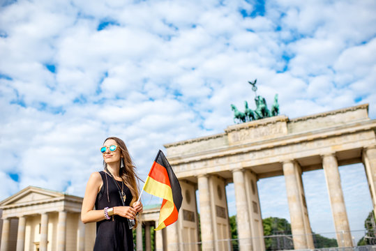 Portrait of a young smiling woman tourist standing with german flag in front of the famous Brandenburg gates in Berlin