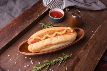 Hot dog with yellow mustard and ketchup on wooden background