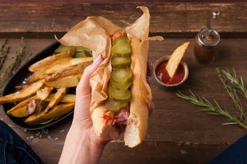 Female hand holding traditional American hot dog on the wooden board. Top view.