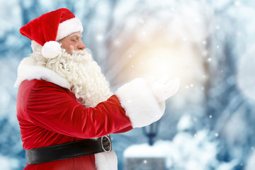 Santa Claus holding magical light in hands on blurred background