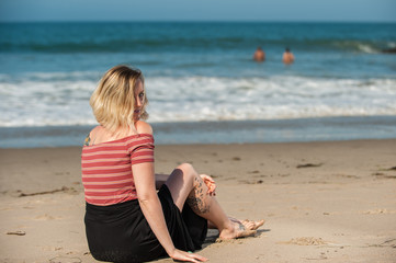 Fototapeta na wymiar Beautiful short hair woman seated on beach sand peeking over shoulder. 
