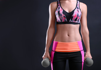 Woman in sport suit holding dumbbells on dark background