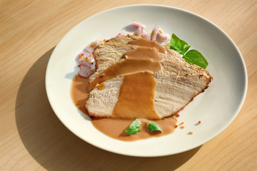 Plate with delicious sliced turkey and sauce on light table