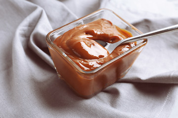Glass bowl with tasty caramel sauce and spoon on table
