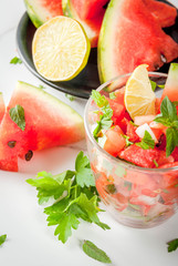 Mexican food. Summer berries and fruits. Vegetable salsa salad with watermelon, tomatoes, onions, greens, lime. In portioned glass on white marble table, with the ingredients. Copy space