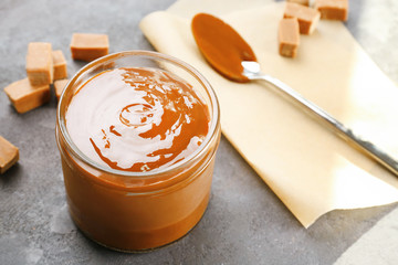 Glass jar with tasty caramel sauce and spoon on table