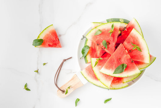 Fresh ripe juicy organic raw watermelon, cut into pieces. On a white marble plate, marble table, with mint leaves. Food background. Copy space