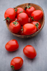Small plum tomatoes in a wooden bowl on a gray background.