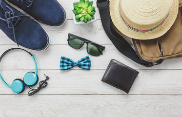 Top view accessoires to travel with man clothing concept. headphone on wooden background.essential items for trip are bow tie,wallet,sunglasses,shoe,bag and hat on wood table.copy space.flat lay.