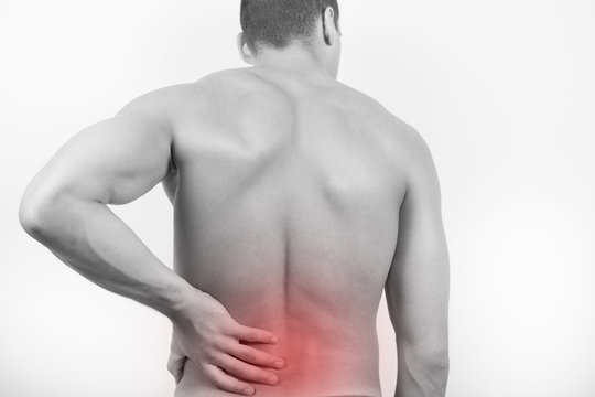 Rear view of a young man holding his back in pain, isolated on white background. Lower back pain. Shirtless man touching his back for the pain.