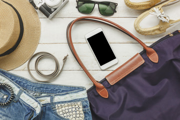 Top view accessoires to travel with women clothing concept.essential items are white mobile phone, belt,bag,hat,camera,necklace,trousers and sunglasses on white wood table.holiday concept.flatlay.
