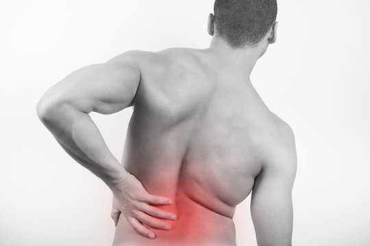 Rear view of a young man holding his back in pain, isolated on white background. Lower back pain. Shirtless man touching his back for the pain.