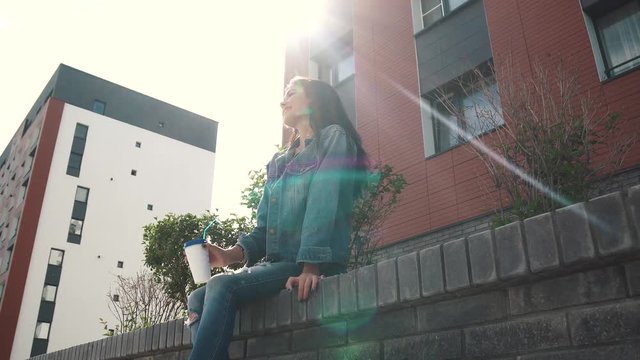 young pretty girl in a denim jacket drinking coffee from a paper Cup on the street