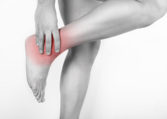 Close up view of a young man holding his ankle in pain, isolated on white background. Lower leg pain. Young man touching his ankle for the pain. Red inflammation effect.
