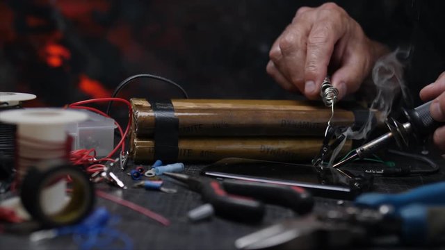 HANDS SOLDERING BOMB CONNECTIONS.  SLOW, CLOSE UP DOLLY MOVE