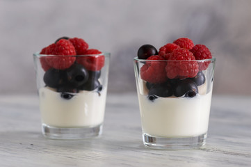 Yogurt with raspberries and black currants in a small Cup on a wooden table. Delicious dessert with berries