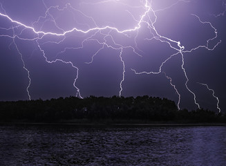 Lightnings at the night over the lake and forest