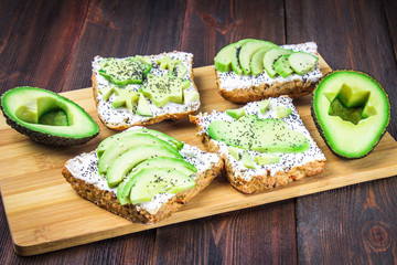 Sandwiches from bread with slices, zvezdami, hearts from avocado and curd cheese on a brown wooden background.