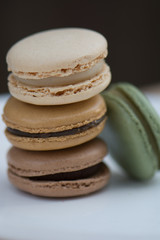 Stack of Four French Macarons on white plate: vanilla, caramel, chocolate, and pistachio