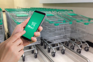 human hand hold and touch shopping application in cell phone on blurry row of cart.