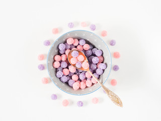 Round purple and pink bonbon candies sweets in gray bowl on white canvas background. Minimal still life