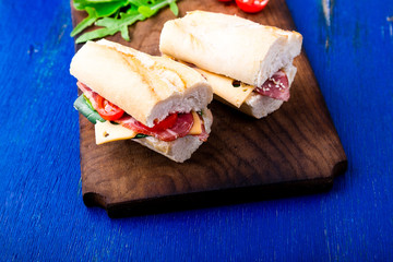 Sandwich with jamon, arugula, tomatoes, cheese on wooden board blue background. Rustic. Two.