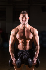 Fototapeta na wymiar Muscular bodybuilder guy doing exercises with dumbbells.