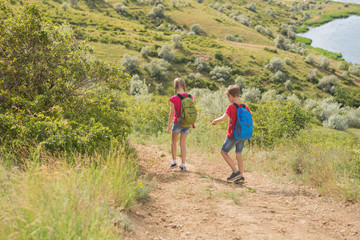 Obraz premium Teen boy and girl with backpacks on the back go on a hike, travel, beautiful landscape